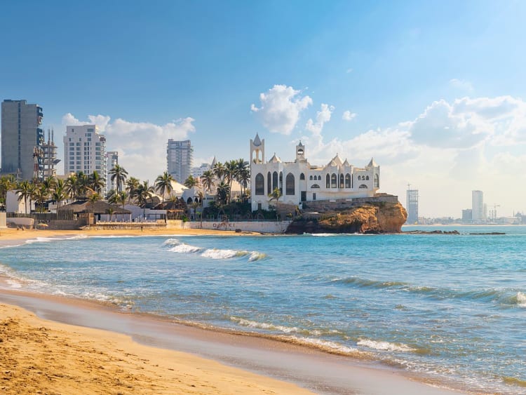Mazatl&aacute;n, Mexiko &ndash; wei&szlig;es K&uuml;stengeb&auml;ude auf Felsen vor Skyline und Palmenstrand