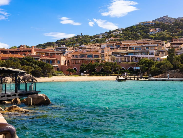 Porto Cervo, Italien &ndash; Rosafarbene H&auml;user am Hang &uuml;ber kristallklarem Wasser
