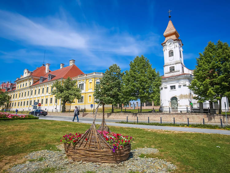 Vukovar, Kroatien &ndash; gelbes Schloss und wei&szlig;e Kirche hinter geflochtenem Blumenkorb