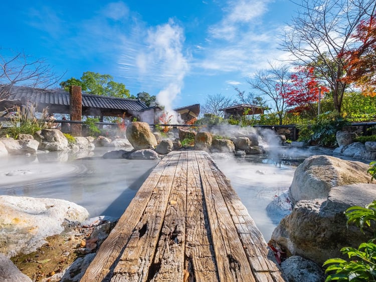 Beppu, Japan &ndash; h&ouml;lzerner Steg &uuml;ber dampfendes Onsen-Becken zwischen Natursteinen