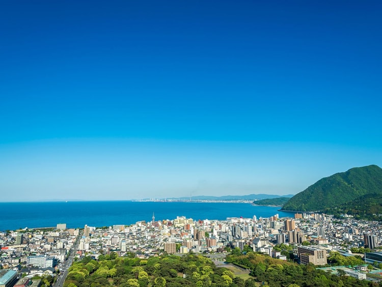 Beppu, Japan &ndash; Blick &uuml;ber die Stadt bis zum Meer und gr&uuml;nem Vulkan im Hintergrund