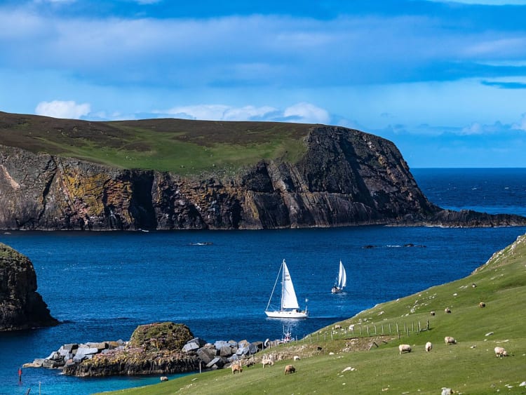 Fair Isle, Schottland &ndash; Felsk&uuml;ste mit wei&szlig;en Segeln im klaren Wasser