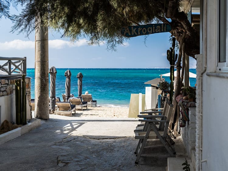 Agia Anna (Naxos), Griechenland &ndash; Zugang zum Strand mit Liegest&uuml;hlen und Sonnenschirmen vor dem t&uuml;rkisblauen Meer.