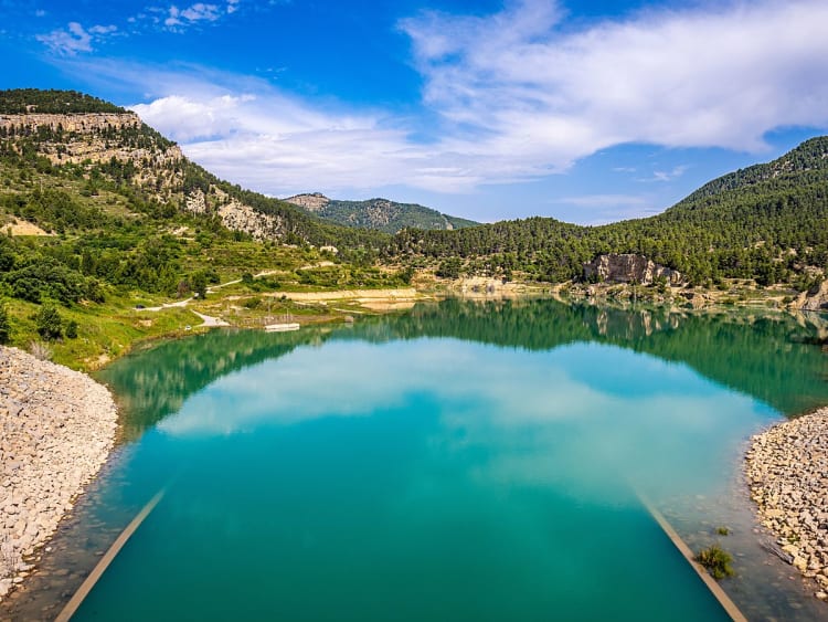 Castell&oacute;n de la Plana (Castell&oacute;n), Spanien &ndash; Ruhiger See in einer bergigen Landschaft mit bewaldeten H&uuml;geln und klarem Himmel.