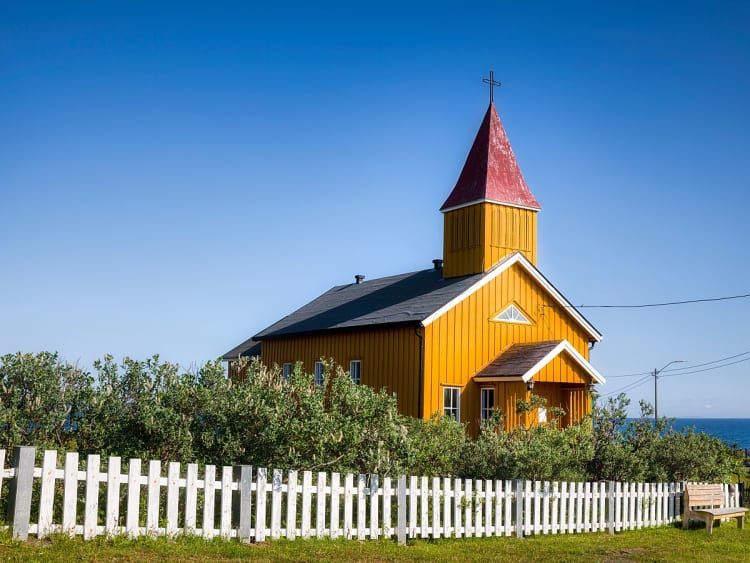 Vads&oslash;, Norwegen - Kirche am Meer mit Zaun, Str&auml;uchern und blauem Himmel