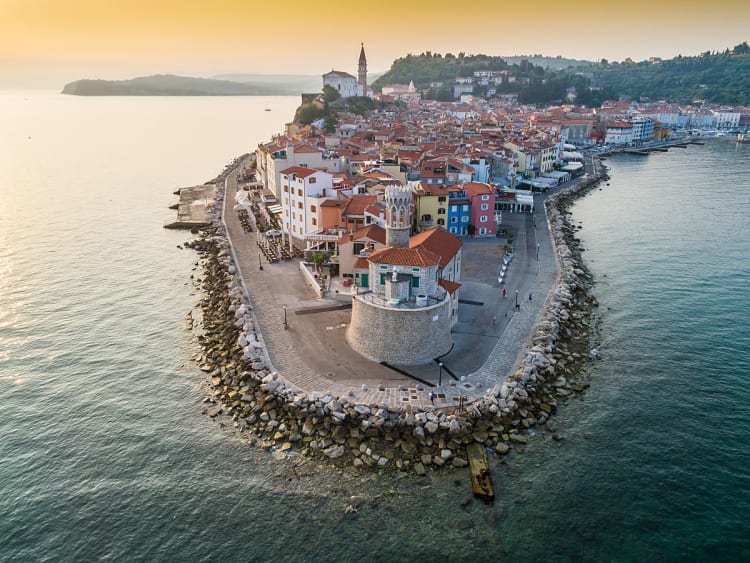 Piran (Slowenien) &ndash; Luftaufnahme der Altstadt auf der Halbinsel mit Leuchtturm, Stadtmauer und Adriak&uuml;ste im warmen Abendlicht
