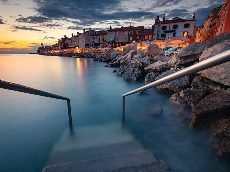 Piran (Slowenien) &ndash; stimmungsvolle Uferpromenade mit bunten H&auml;usern und Restaurants bei Sonnenuntergang, Blick &uuml;ber die Adria