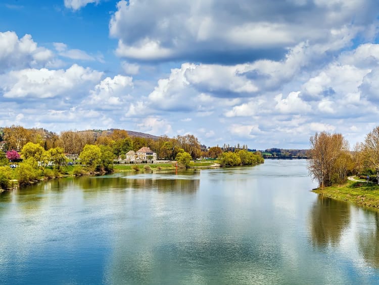 Tournus (Frankreich) - Ruhiger Fluss mit gr&uuml;nen Ufern und B&auml;umen unter wolkigem Himmel