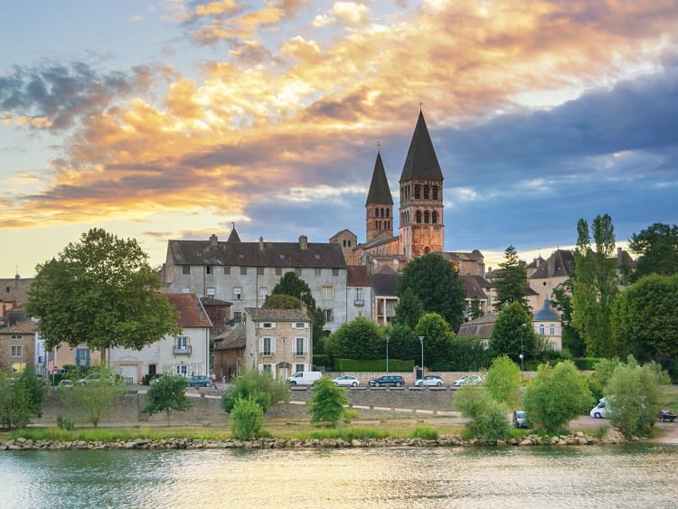Tournus (Frankreich) - Kirche mit zwei T&uuml;rmen &uuml;ber H&auml;usern am Fluss bei Sonnenuntergang