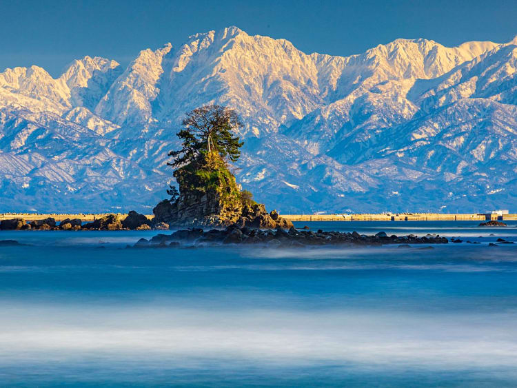 Toyama, Japan &ndash; Rocky islet against a backdrop of snow-capped mountains