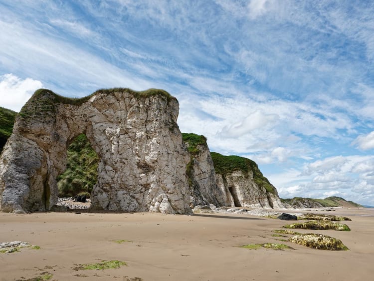 Portrush, Noord-Ierland &ndash; Begroeide kustrotsen onder een blauwe hemel