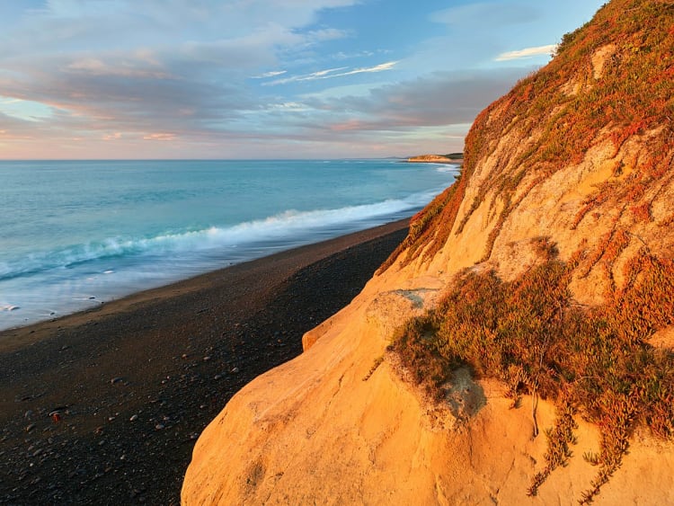 Timaru, Nouvelle-Z&eacute;lande &ndash; Plage sombre au pied de falaises baign&eacute;es de lumi&egrave;re dor&eacute;e