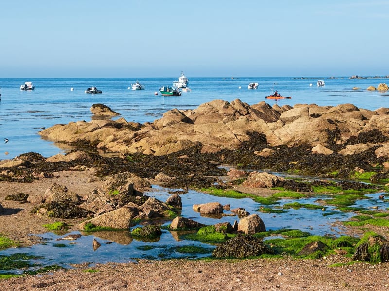 Cherbourg, Frankreich &ndash; Felsige K&uuml;ste bei Ebbe mit Booten auf ruhiger See im Hintergrund