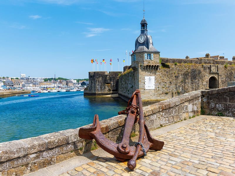 Concarneau, Frankreich &ndash; Historische Festungsmauern mit Uhrturm und gro&szlig;em Anker am Hafen