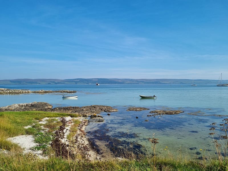 Gigha, Schottland &ndash; Ruhige K&uuml;stenbucht mit kleinen Booten auf klarem Wasser und Blick auf die sanften H&uuml;gel der Hebriden.