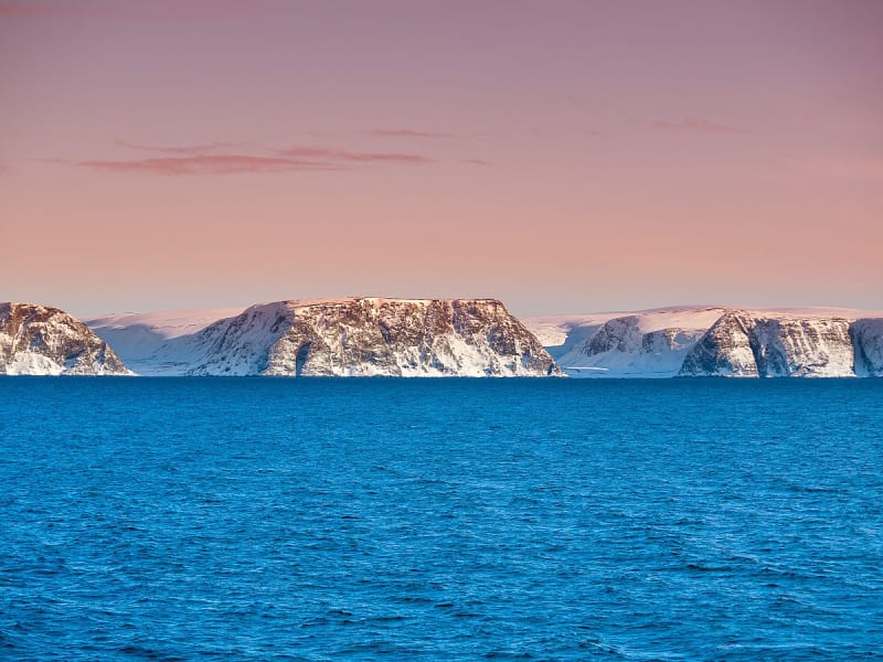 Kj&oslash;llefjord, Norwegen - Schneebedeckte Klippen am Meer unter rosafarbenem Himmel