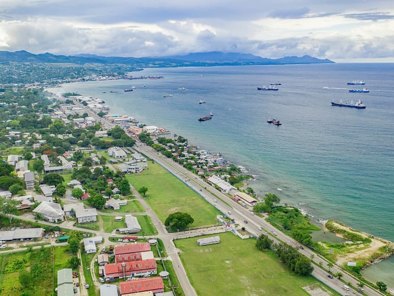Honiara (Guadalcanal, Salomonen) - K&uuml;stenstra&szlig;e mit H&auml;usern und Schiffen in weiter Bucht