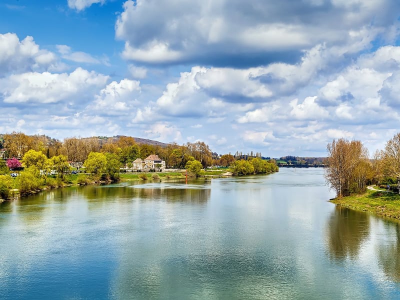 Tournus (Frankreich) - Ruhiger Fluss mit gr&uuml;nen Ufern und B&auml;umen unter wolkigem Himmel