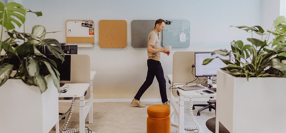 Ein Mitarbeitender läuft mit einem Kaffee zu seinem Arbeitsplatz.