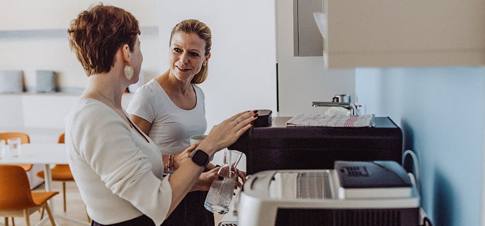 Zwei Mitarbeitende unterhalten sich in der Kaffee-Küche.
