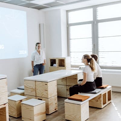 Zwei Mitarbeitende hören bei einem Meeting in einem hellen Raum zu