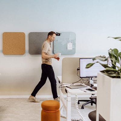 Ein Mitarbeitender läuft mit einem Kaffee zum Arbeitstisch