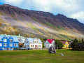 Ísafjörður, Island – Farbige Holzhäuser vor steil aufragender Bergwand