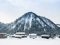 Sakata, Japan - Verschneites Dorf vor bewaldetem Berg unter grauem Winterhimmel