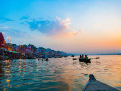 Boote und Badende am Flussufer des Ganges in warmem Abendlicht und bunter Stimmung