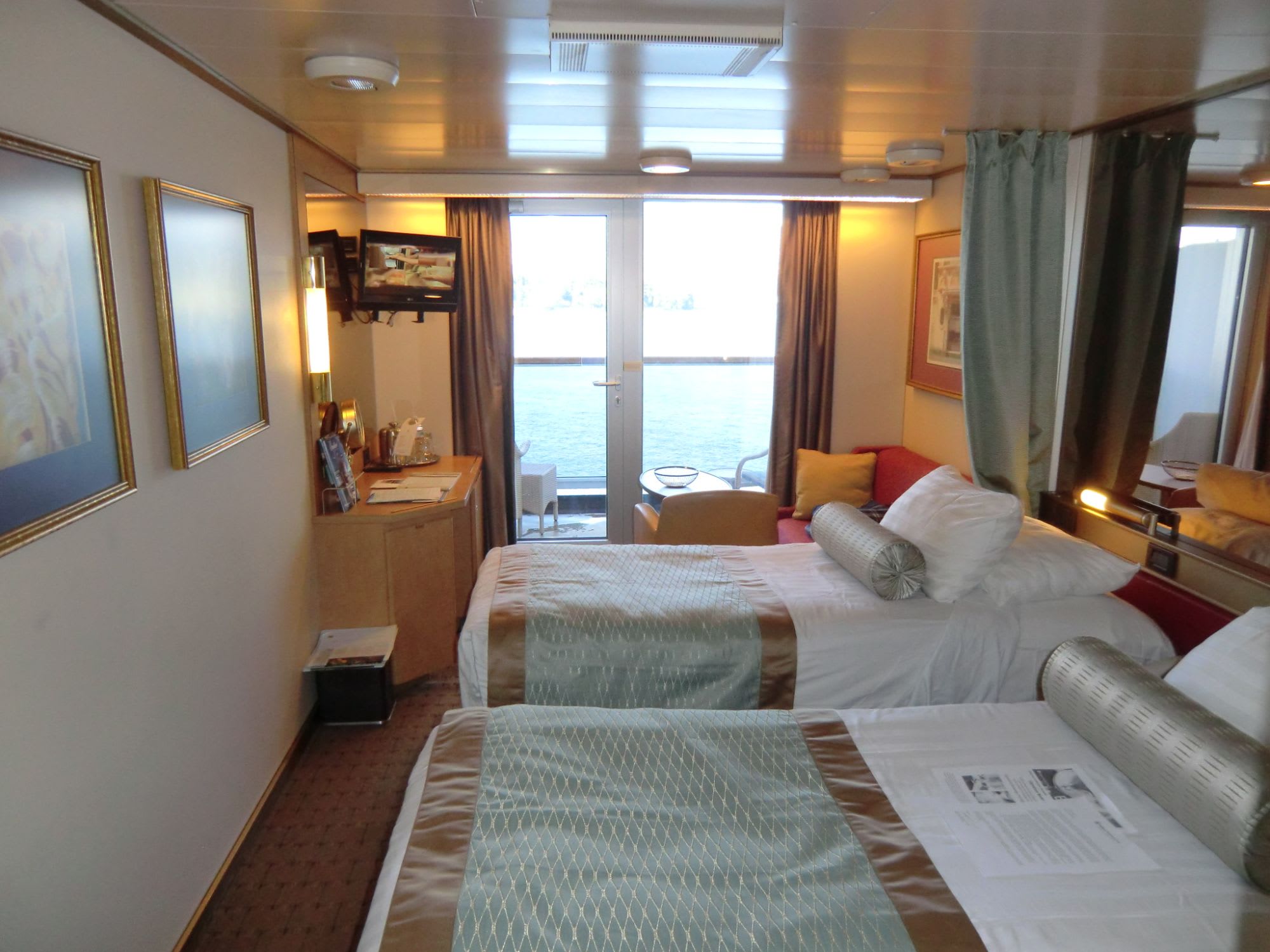 –我々の客室–　■海側バルコニー■内装は白を基調とし、上品で落ち着きがある。窓側にふらっとテレビとデスク、２人用のソファ