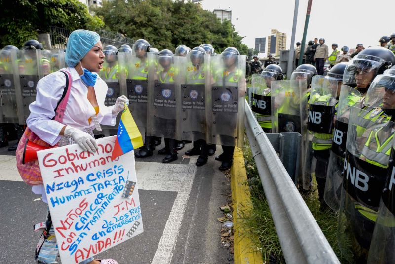 A health care worker carrying a banner confronts police agents during a demonstration against President Nicolas Maduro's government, the lack of medicines and low salaries in the country, in Caracas on February 7, 2017.