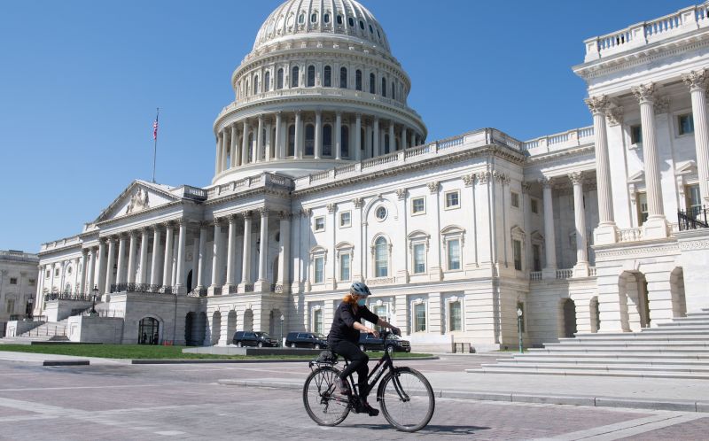 A woman wearing a mask to prevent the spread of COVID-19, known as coronavirus, rides a bike in front of the US Capitol in Washington, DC, April 9, 2020. 