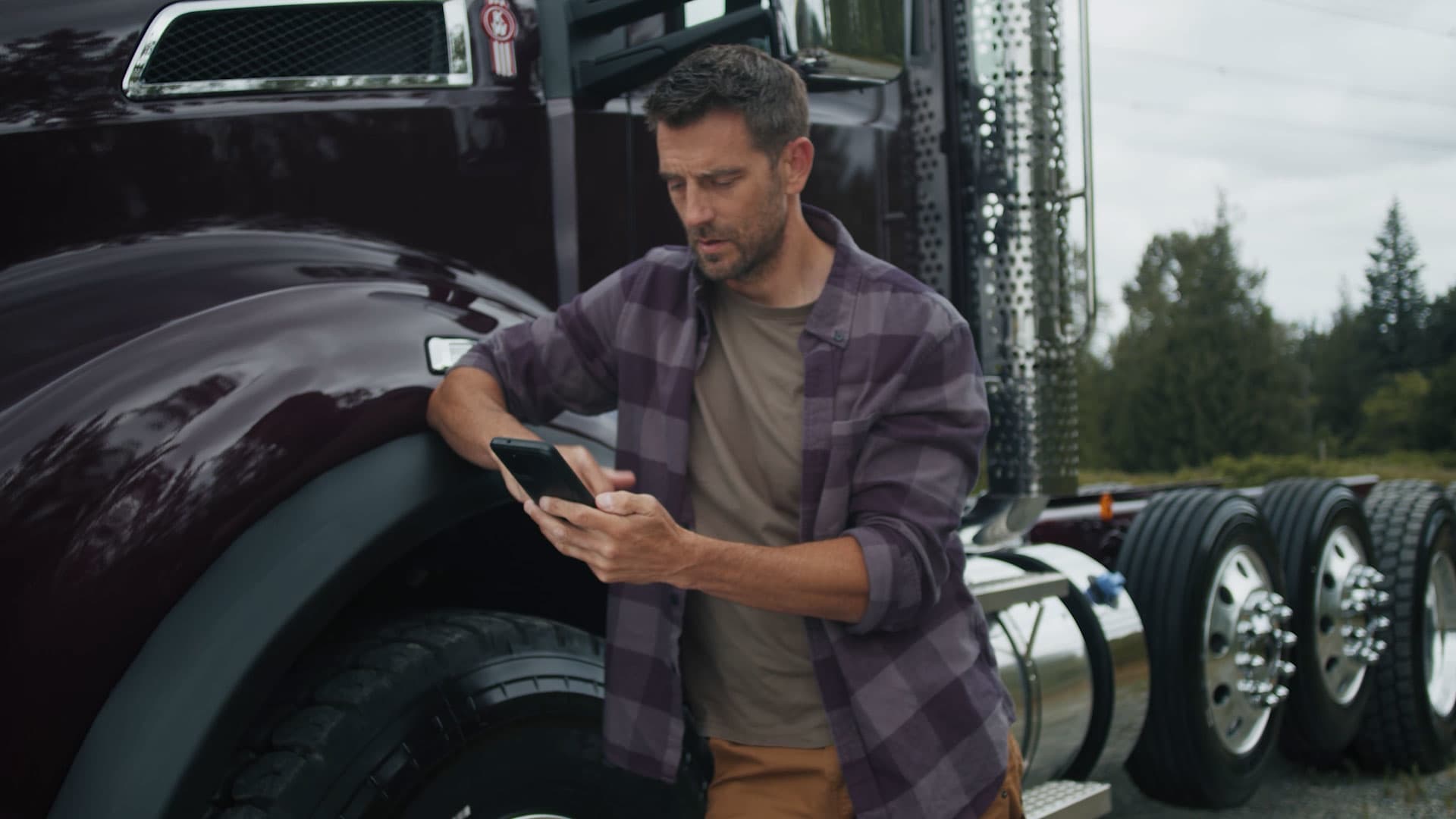A man looking at his phone standing by Kenworth truck looking for a dealership
