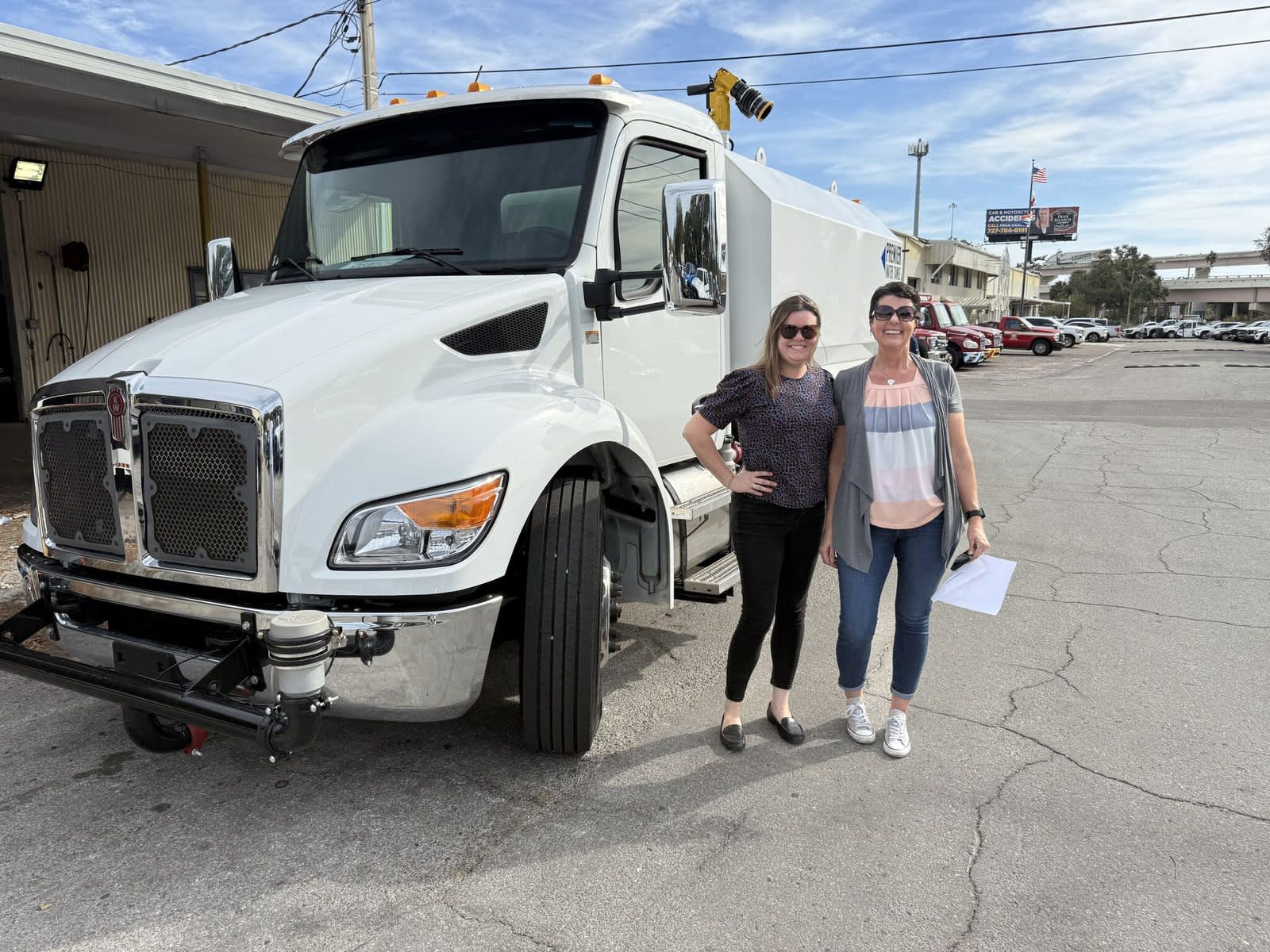 Customer delivery at Florida Kenworth featuring a white Kenworth service truck parked outside the dealership with two individuals standing alongside the vehicle.