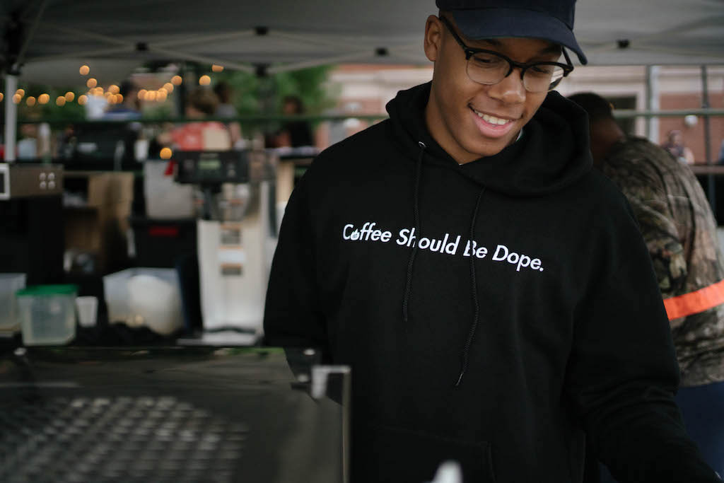 Barista wearing a hoodie saying 'Coffee Should Be Dope.'