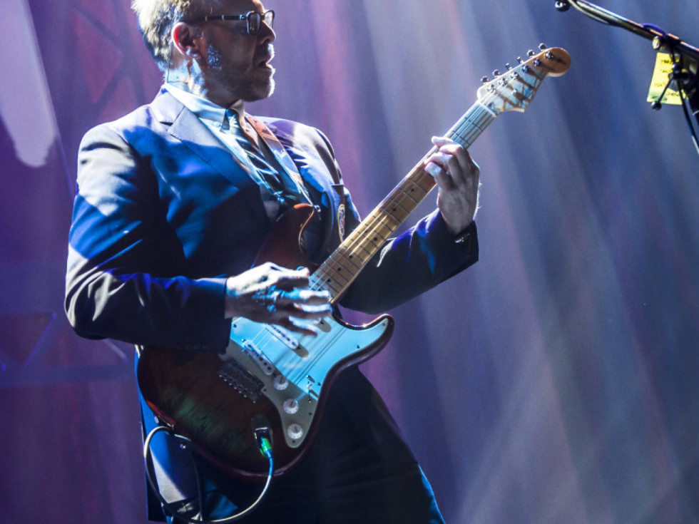 Alton Brown plays an electric guitar onstage.