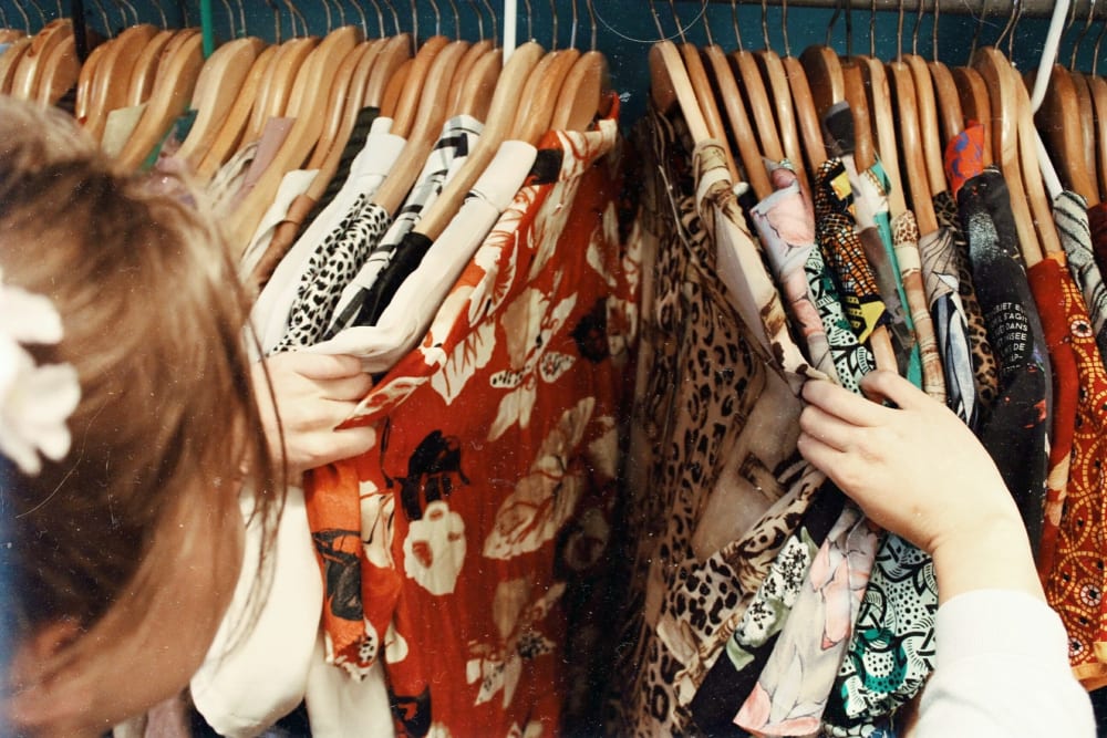 Woman shifts through a collection of colourful vintage shirts on a rail