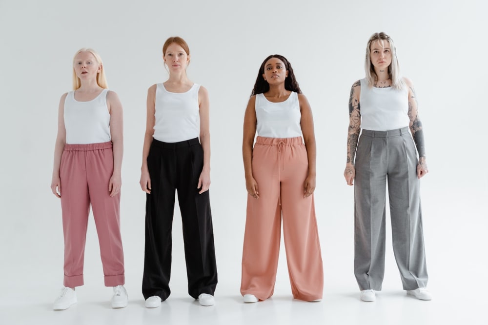 Four women of different shapes and sizes wearing white tucked in tank tops