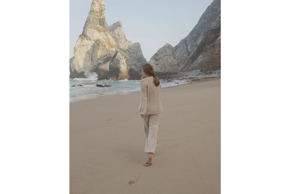 Woman running barefoot on a beach with her back to the camera wearing a selection of woollen garments