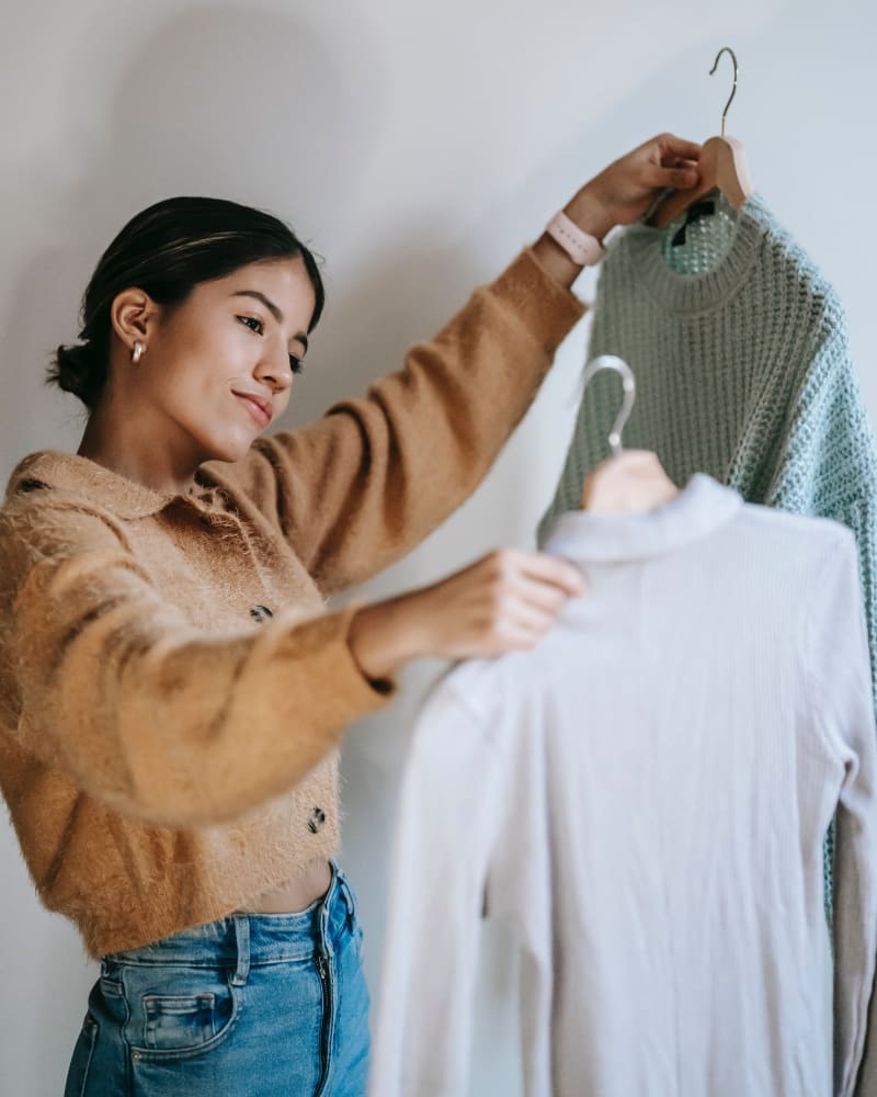 A young woman deciding on which top to wear on hangers