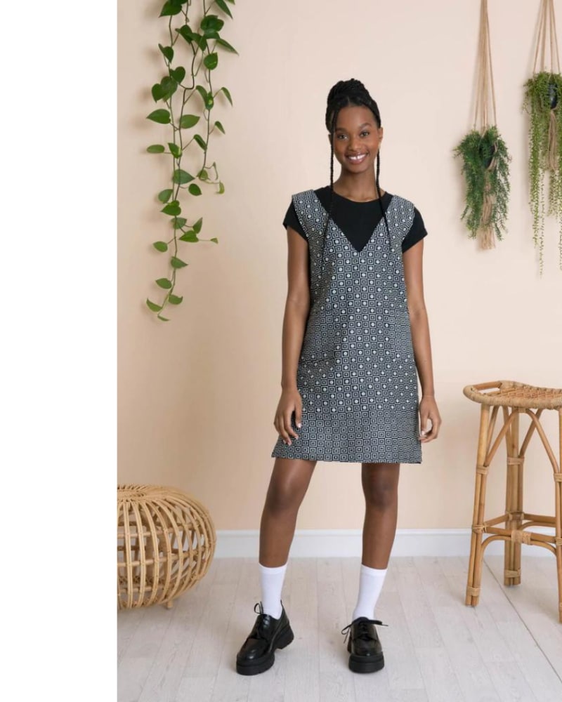 Female model wearing a light grey patterned a-line dress with a deep v neck line and a black t-shirt underneath