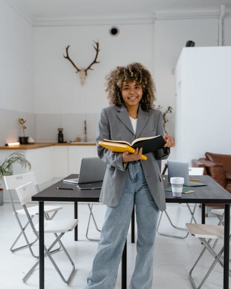 A woman, wearing a grey blazer and blue jeans, holding books