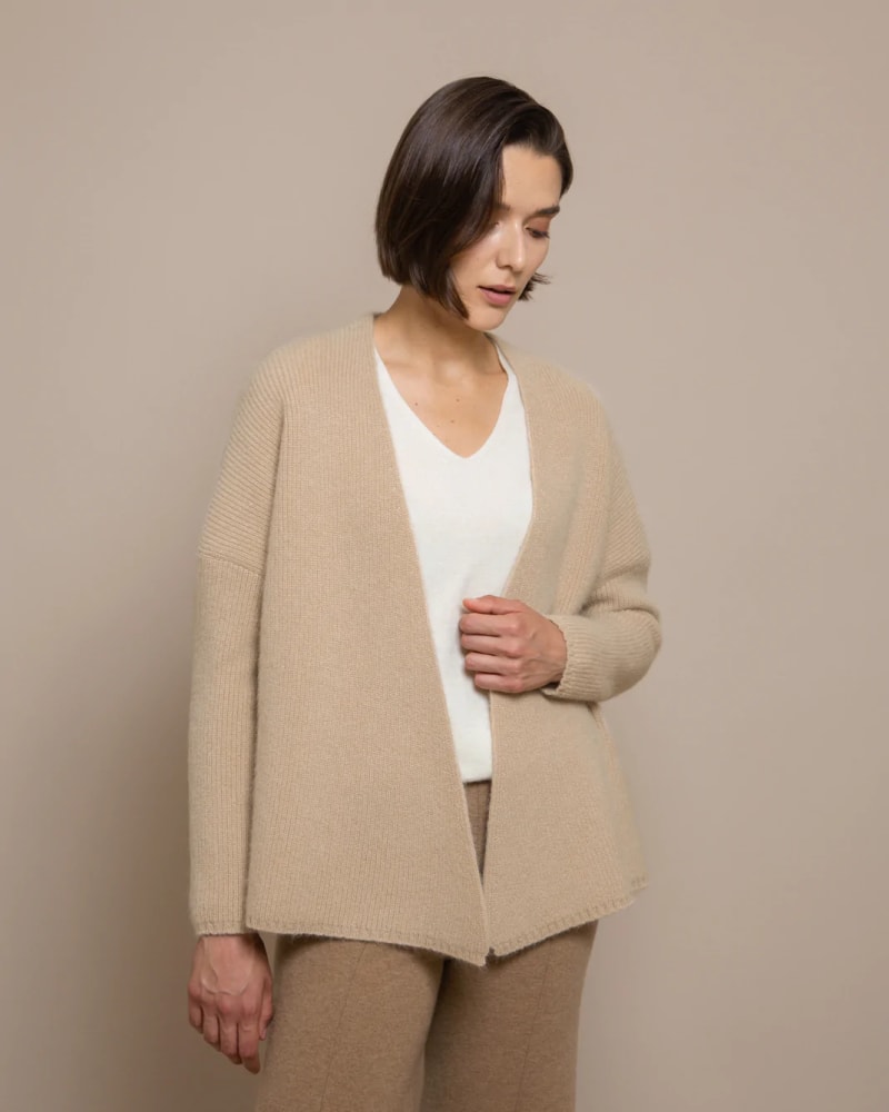 Woman wearing a beige coloured cardigan, with a white top and dark beige trousers