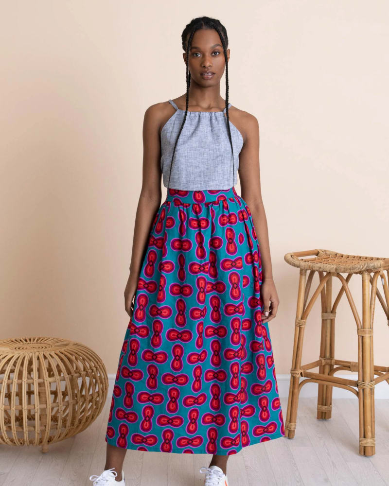 A woman standing with a light blue halter neck top; a darker blue maxi skirt with a pink and purple turtle pattern on it