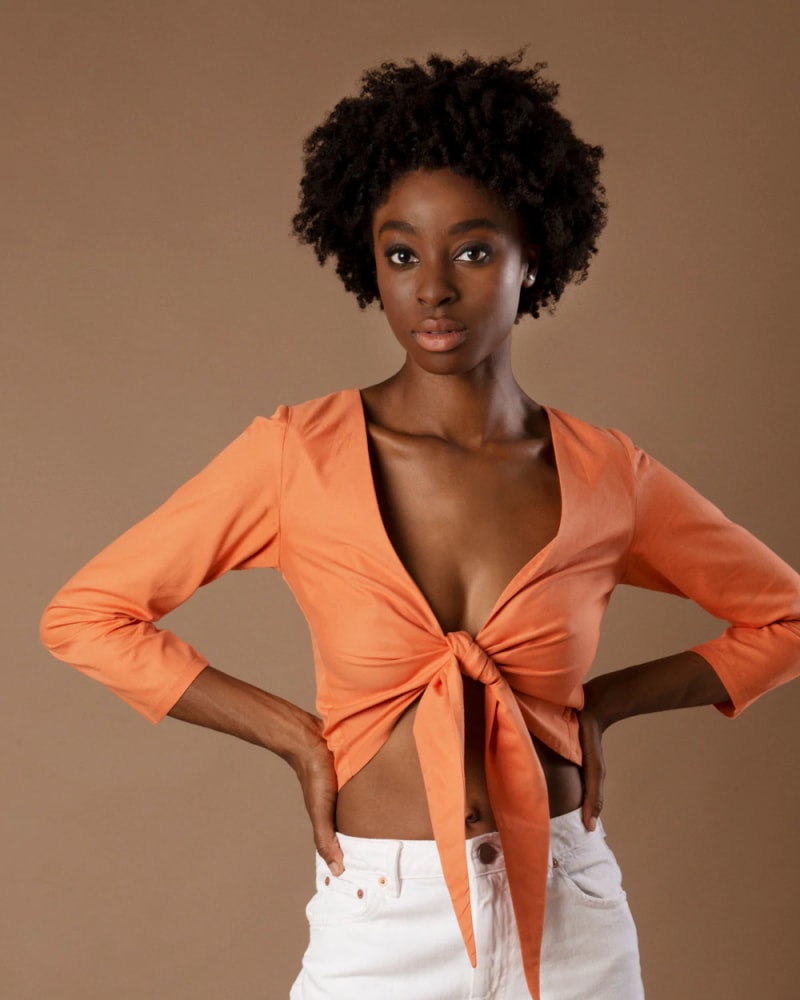 Women wearing an orange, three-quarter sleeved cropped shirt which ties at the front.