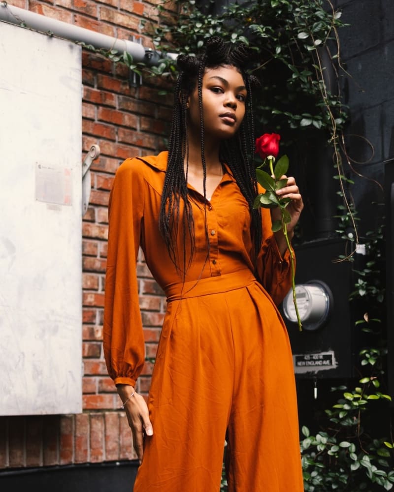 Woman wearing a one-piece wide legged jumpsuit in heels holding a red rose