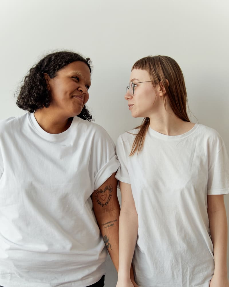 Two woman holding hands, both wearing white t-shirts of a different fit