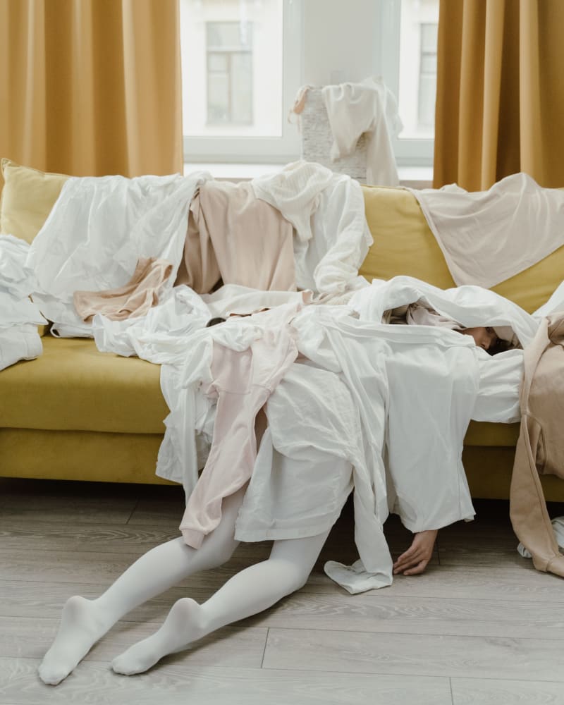 We've all been there - the spring clean mayhem! Woman laying underneath a pile of unorganised clothing