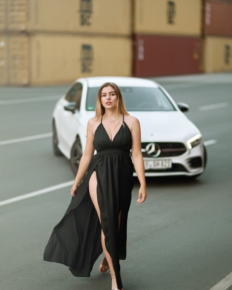 Woman walking down the road in a black plunge maxi dress with spaghetti straps and a hip height side slit