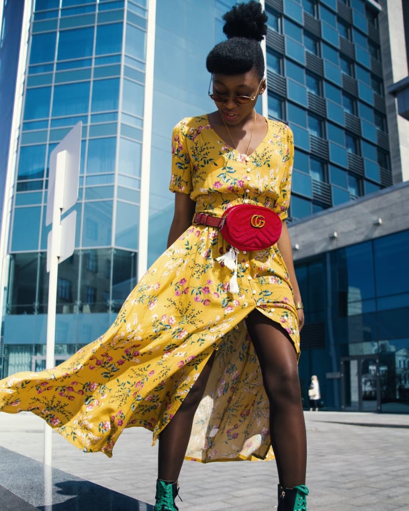 Woman in a yellow floral dress, sunglasses and a red Gucci purse with green laced boots